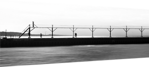 Couple strolling along The Pier in Black and White, with a bird flying and a smokestack in the distance.