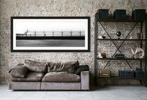 A couple strolls along The Pier in Black and White, with a bird flying nearby and a smokestack in the distance.